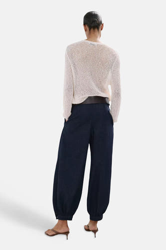 Jean en denim bleu marine à jambes ballon de MANGO, avec poignets élastiques, porté avec un pull en maille de couleur crème, une ceinture marron et des sandales marron.
