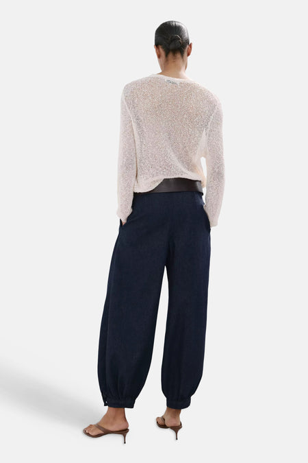 Jean en denim bleu marine à jambes ballon de MANGO, avec poignets élastiques, porté avec un pull en maille de couleur crème, une ceinture marron et des sandales marron.