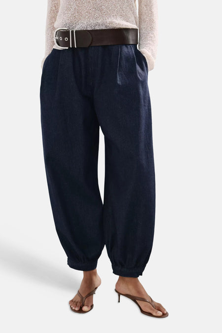 Jean en denim bleu marine de MANGO avec plis, jambes larges et chevilles plissées, stylisé avec une ceinture et des sandales.