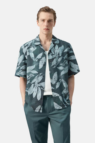 Kort mouwen hemd in donkergroen met lichtgrijze bladeren van MANGO, met gerimpelde textuur, open kraag, gedragen over een wit T-shirt en bijpassende broek.