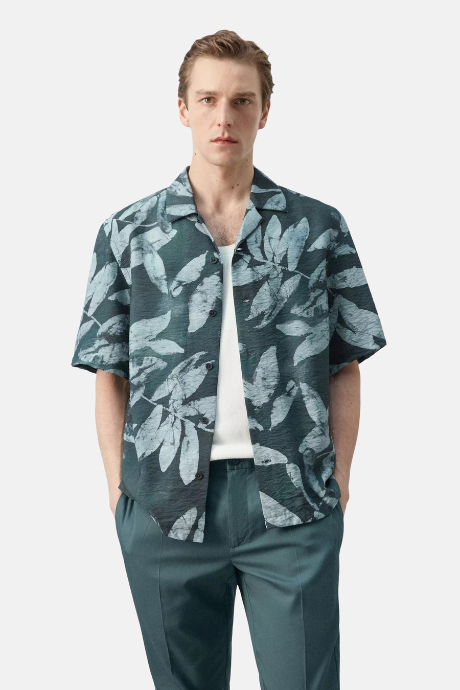 Kort mouwen hemd in donkergroen met lichtgrijze bladeren van MANGO, met gerimpelde textuur, open kraag, gedragen over een wit T-shirt en bijpassende broek.