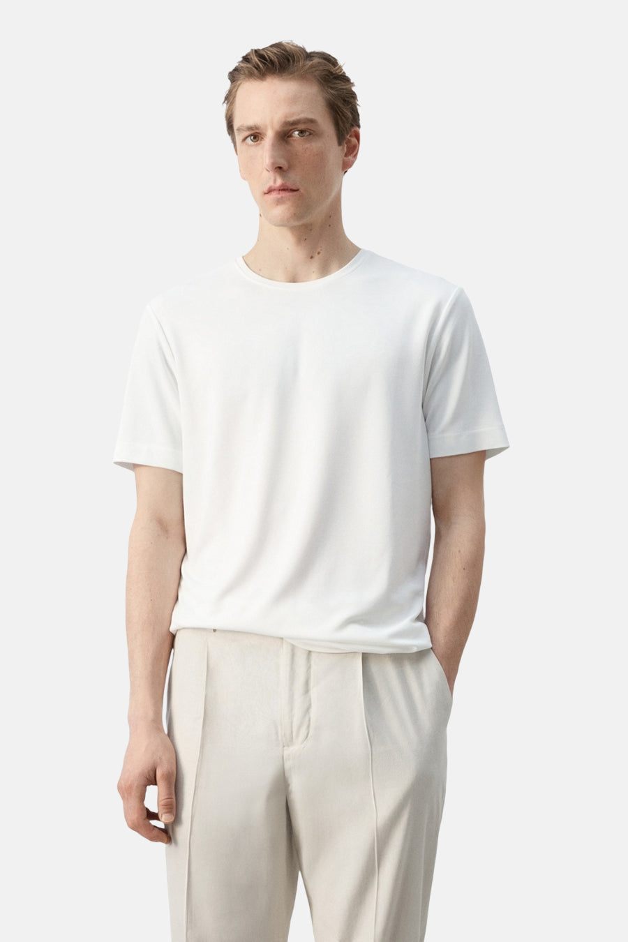 Wit T-shirt met korte mouwen van MANGO, gedragen door een man met een lichte plooibroek.