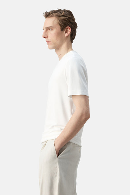 Wit T-shirt met korte mouwen van MANGO, gedragen door een man in zijprofiel met lichte broek.