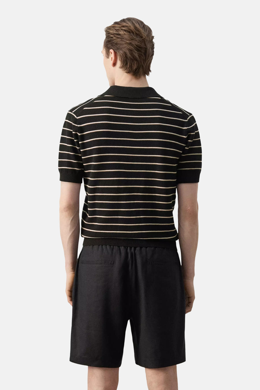 Zwarte polo van MANGO met fijne horizontale lichte strepen, korte mouwen en kraag, van achteren gezien gedragen met een zwarte korte broek.