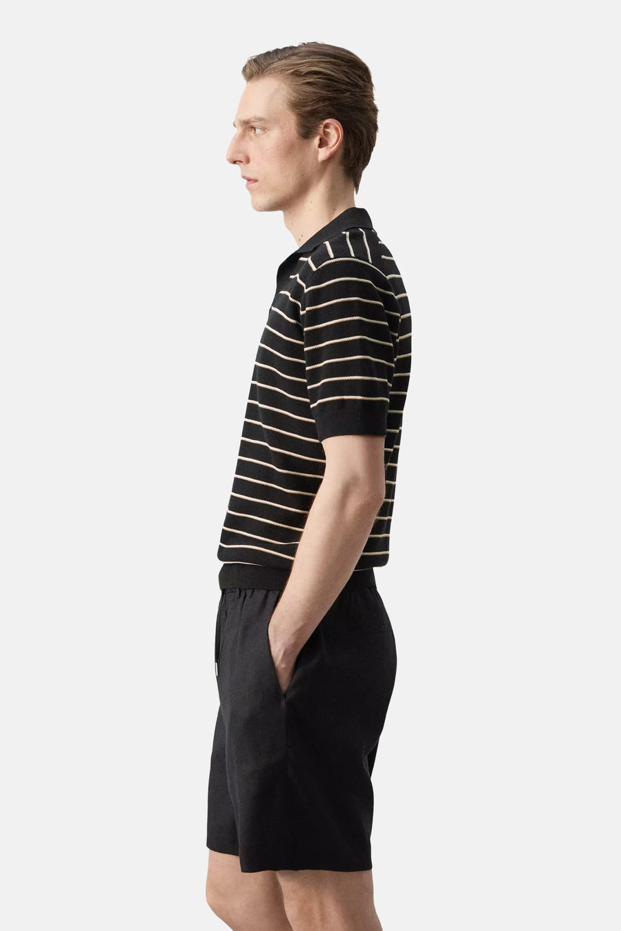 Polo rayée noire de MANGO avec rayures blanc cassé et manches courtes, portée avec un short noir.