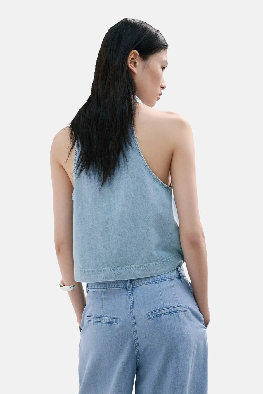 Lichtblauwe denim mouwloze blouse van MANGO, rugzijde met diepe V-hals, gestreept detail, model in denim broek, zilveren armband