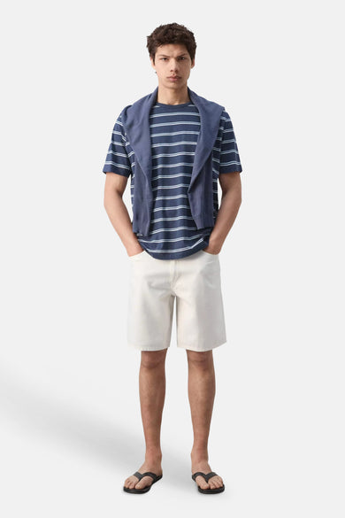 Blauw gestreept T-shirt van MANGO, gedragen met een trui over de schouders, witte shorts en teenslippers.
