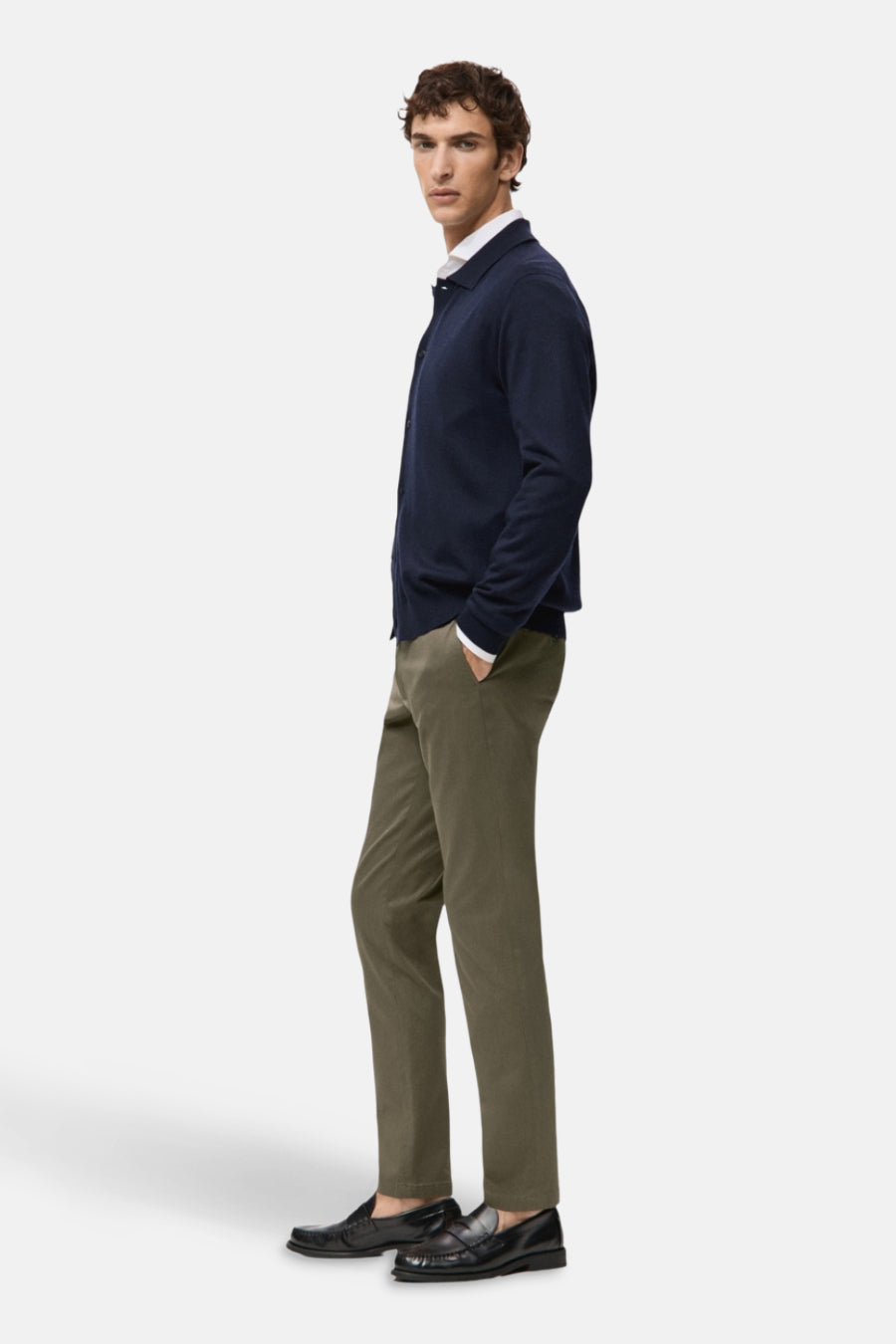 Chino vert de MANGO, associé à un veston bleu et des loafers noirs, debout dans une position latérale.