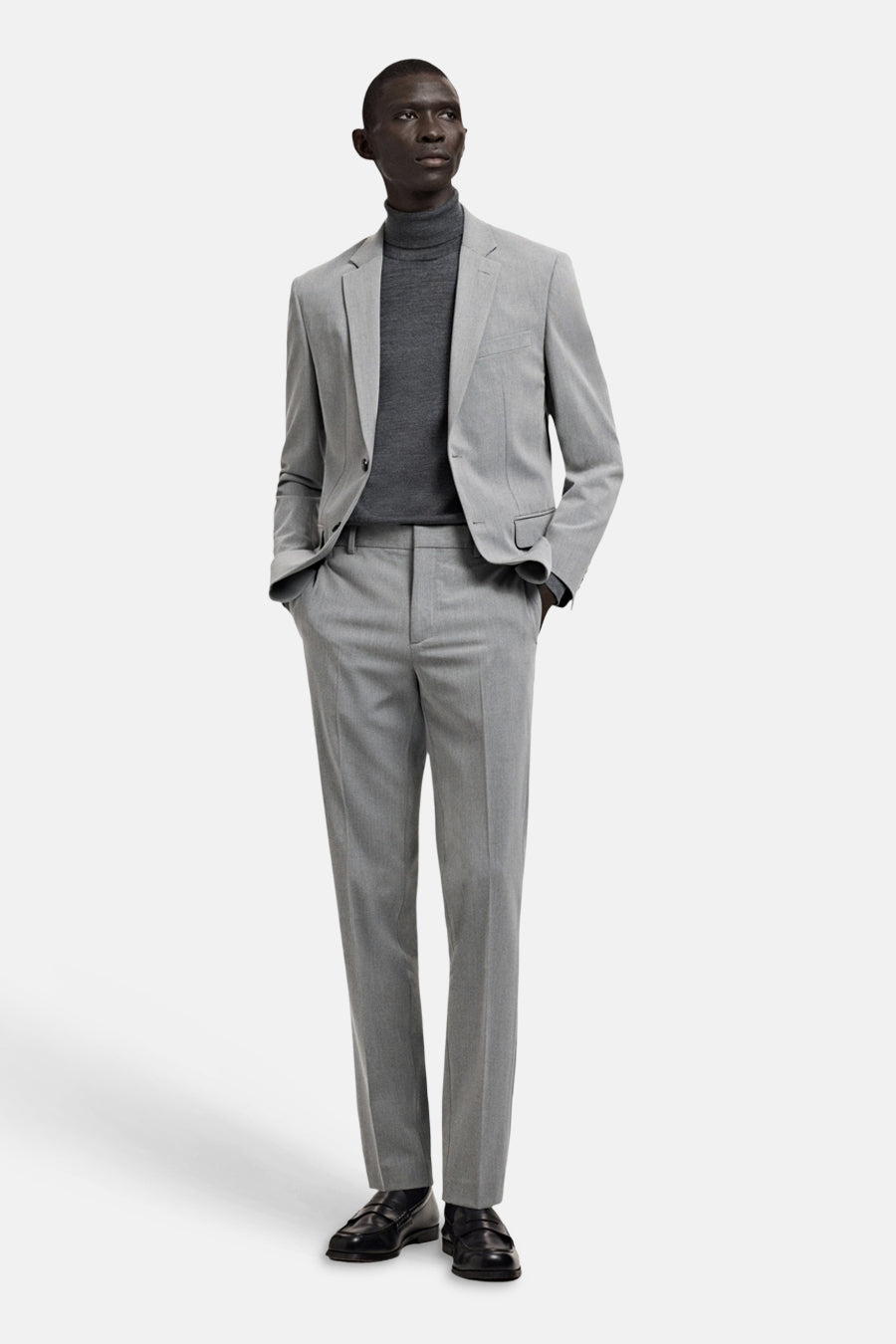 Grijze blazer van MANGO, gedragen met een grijze coltrui en een bijpassende pantalon, gecombineerd met zwarte schoenen.
