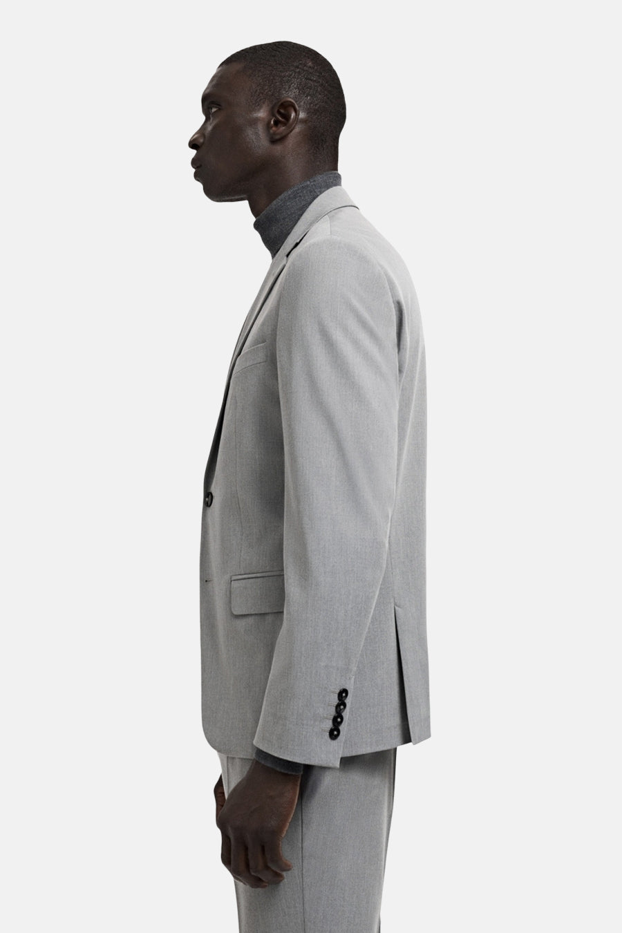 Grijze blazer van MANGO, gezien vanaf de zijkant, met lange mouwen en een grijze coltrui eronder.
