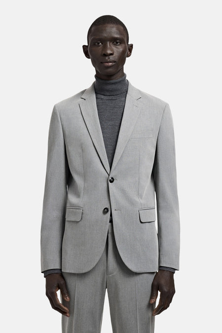 Grijze blazer van MANGO, met een enkele knoopsluiting en zakken met klep, gedragen over een grijze coltrui.
