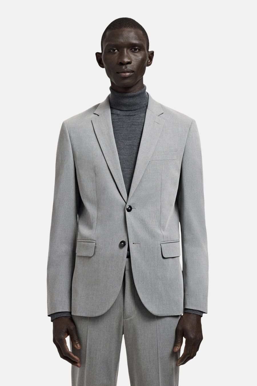 Grijze blazer van MANGO, met een enkele knoopsluiting en zakken met klep, gedragen over een grijze coltrui.
