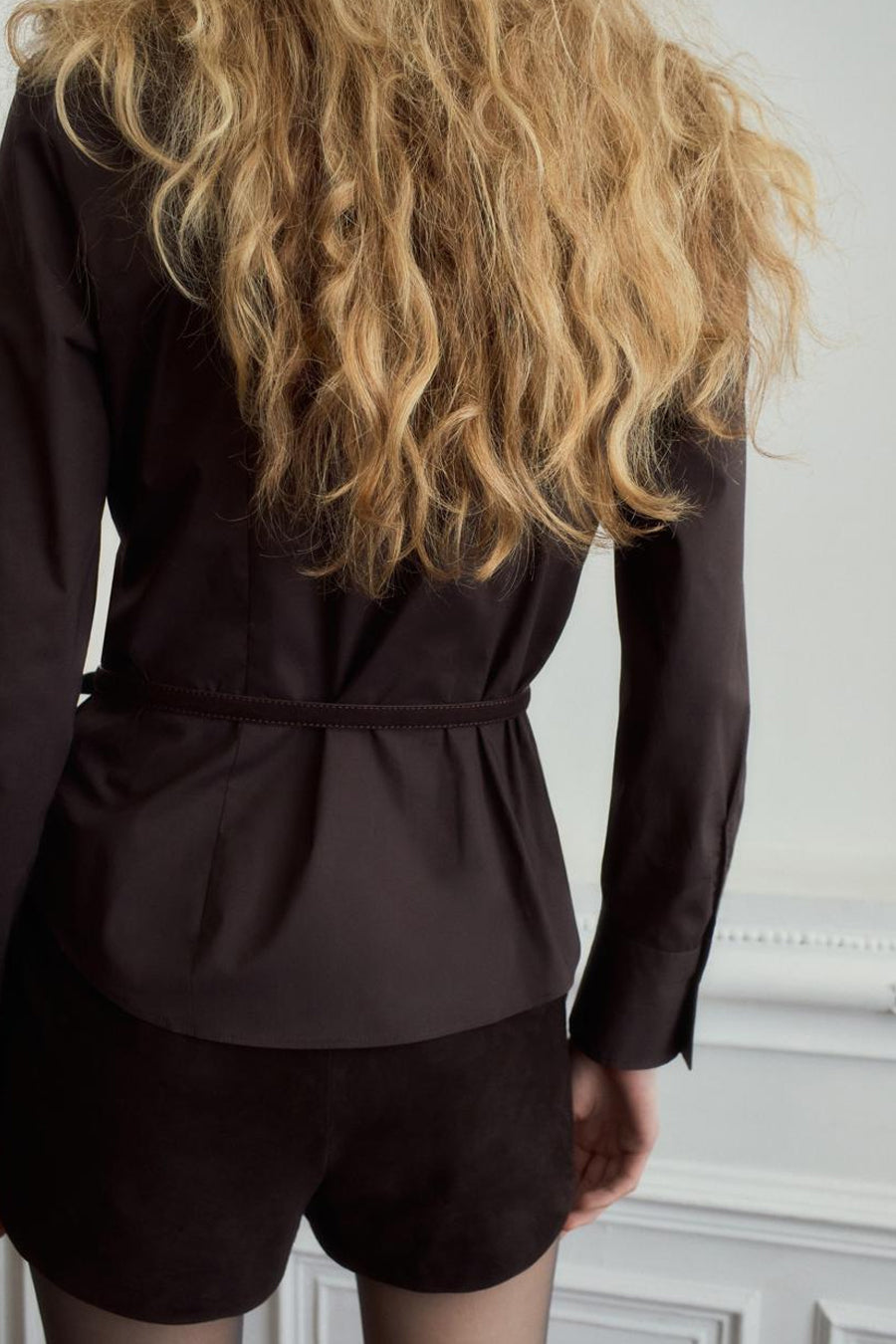 Bruin hemd met lange mouwen van MANGO, gezien van achteren met riem in de taille en krullend blond haar.
