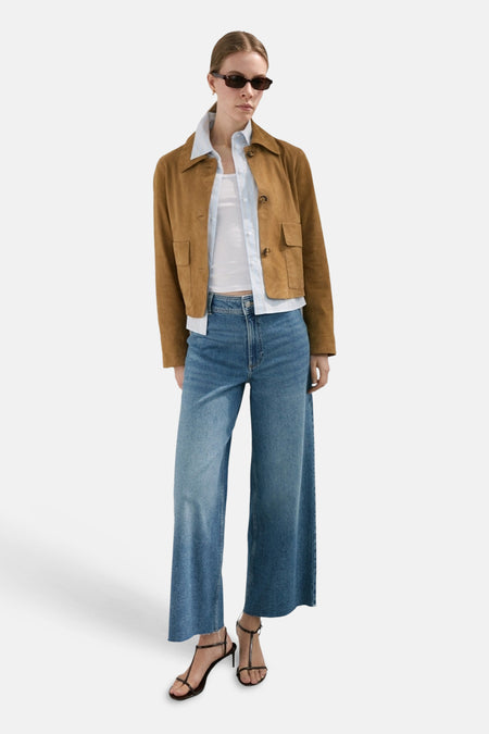 Jean large en denim bleu moyen de MANGO, associé à une veste marron et des sandales noires.