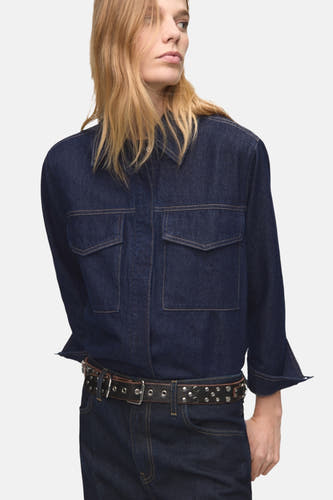 Donkerblauw denim overhemd met lange mouwen van MANGO, met borstzakken en een zwarte leren riem met studs.

