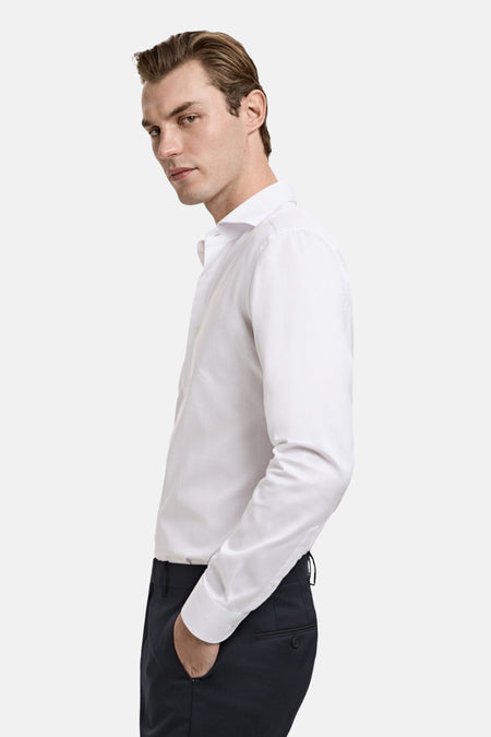 Chemise blanche à manches longues de MANGO, avec un col classique et portée avec un pantalon foncé.