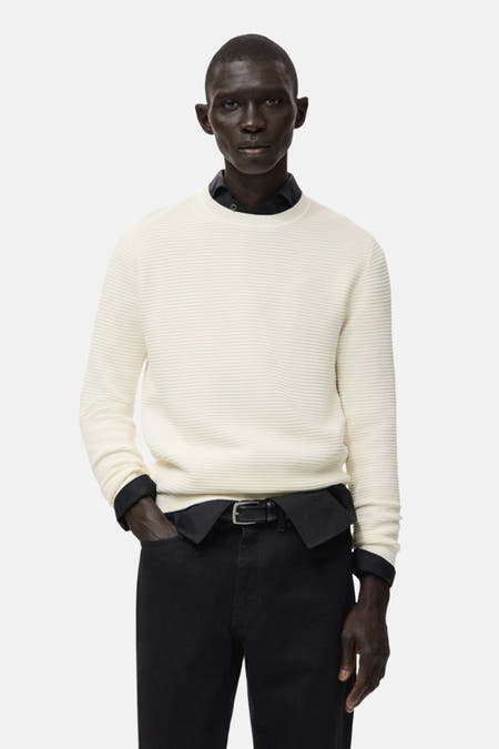 Ecru pull met ronde hals van MANGO, gedragen over een zwart overhemd en gecombineerd met een zwarte broek.
