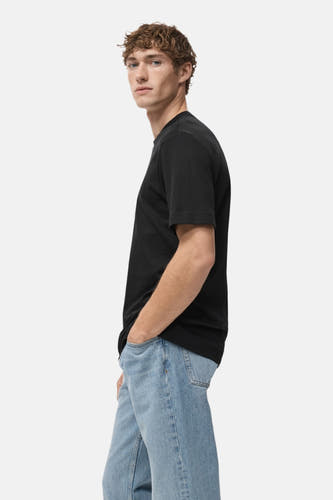 Zwart T-shirt met korte mouwen van MANGO, met model in lichtblauwe jeans, zijaanzicht.
