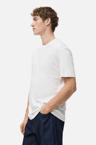 Wit T-shirt met korte mouwen van MANGO, gedragen met donkere jeans, zijdelings weergegeven.