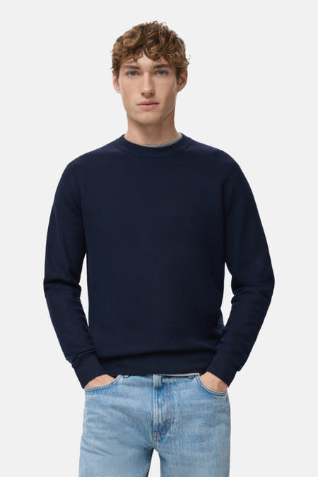 Blauwe trui met ronde hals van MANGO, gedragen met een grijs shirt eronder en een lichtblauwe jeans.
