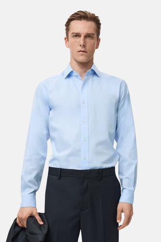 Chemise bleue à manches longues de MANGO, vue de derrière, associée à un pantalon foncé et une veste.