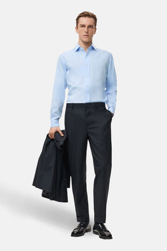 Chemise bleue à manches longues de MANGO, portée avec un pantalon noir et des chaussures, tenant un colbert dans la main.