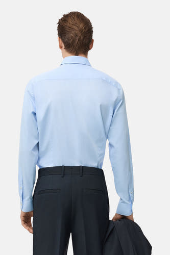 Blauw overhemd met lange mouwen van MANGO, achterkant gezien, gecombineerd met donkere pantalon en een jas.
