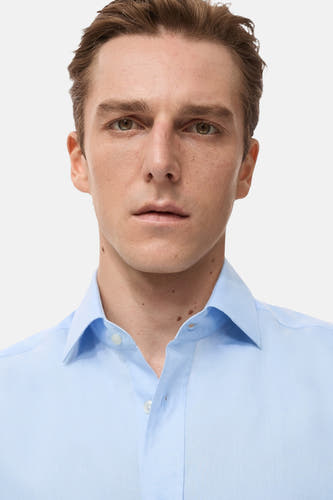 Chemise bleue à manches longues de MANGO, unie et portée avec un col ouvert.