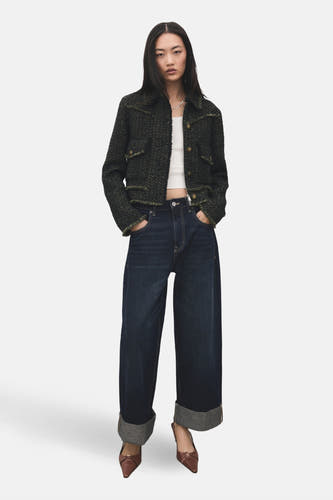 Blazer vert de MANGO, avec un motif tweed texturé et des boutons dorés, associé à une chemise blanche et des jeans larges.
