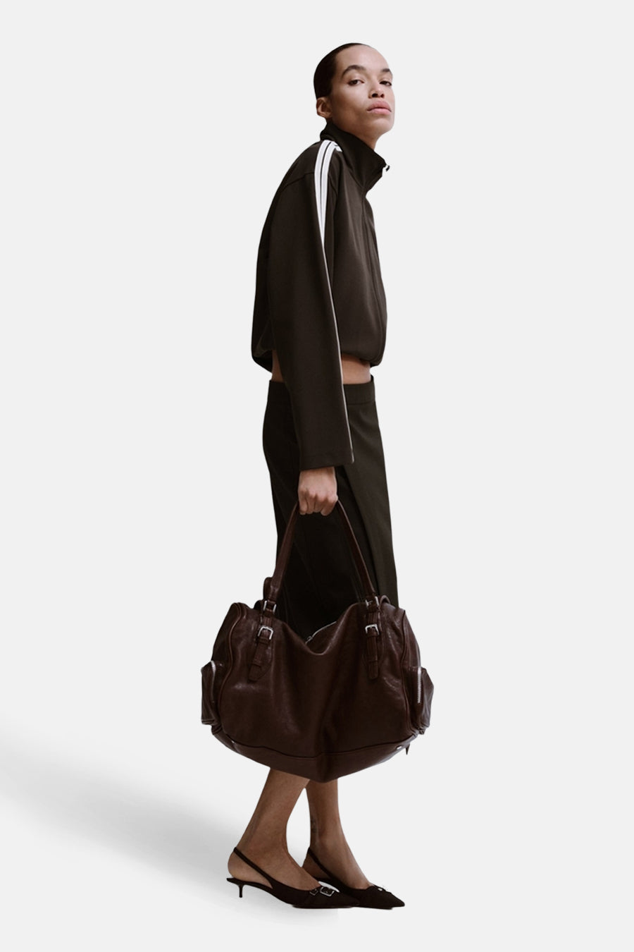 Gilet marron de MANGO porté avec un pantalon d'entraînement foncé et des rayures blanches et une poche marron.