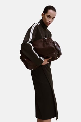Gilet marron de MANGO, porté sur une chemise noire et une jupe, avec un sac à main en cuir marron.