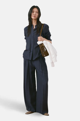 Blauw overhemd met lange mouwen van MANGO, met een krijtstreeppatroon, gedragen met een bijpassende broek en een bruine tas.
