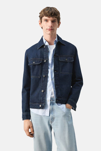 Veste en jean bleu marine de MANGO, vue de dos, portée avec une chemise rayée et un jean clair.