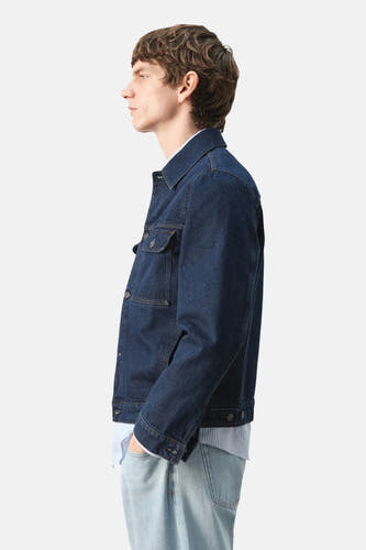 Veste en jean de couleur bleu foncé en denim de MANGO, vue de côté avec poches poitrine et jean bleu clair.