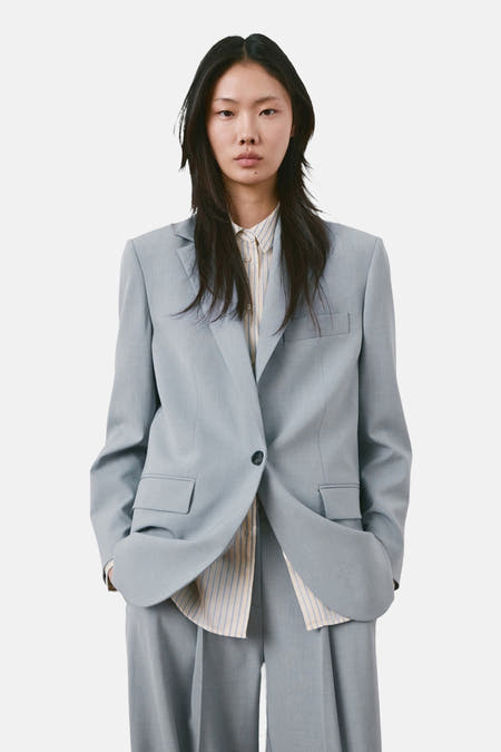 Blauwe blazer van MANGO, gedragen over een gestreept overhemd en een broek in dezelfde kleur.
