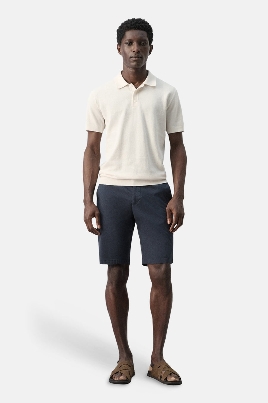 Ecru poloshirt van MANGO, gecombineerd met marineblauwe shorts en bruine sandalen.