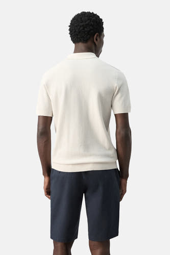 Ecru polo van MANGO, achterkant, met korte mouwen en donkerblauwe shorts.