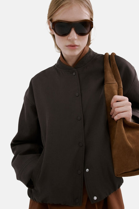 Blazer marron de MANGO, porté avec une blouse orange et un pantalon à carreaux, combiné avec un sac marron.