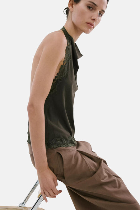 Haut à licou kaki de MANGO avec col drapé et finition en dentelle, porté avec un pantalon plissé marron et des sandales noires.