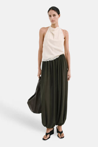 Haut sans manches écru à col licou, col drapé et bordure en dentelle de MANGO, portée avec un pantalon vert foncé et des sandales noires.