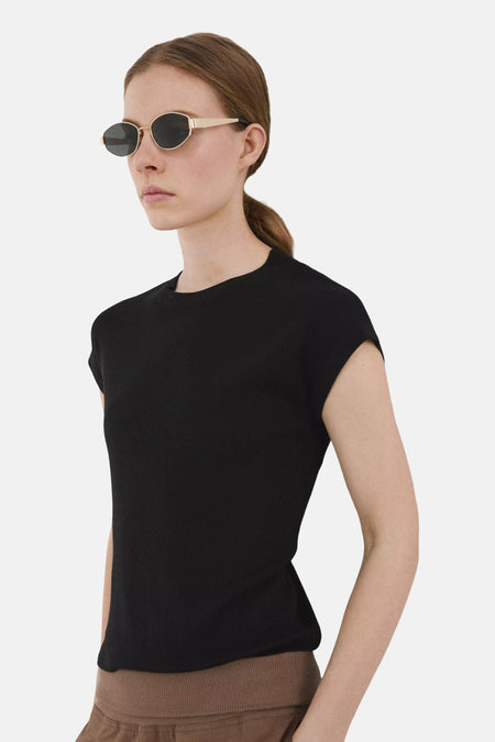 Haut noire de MANGO à manches courtes et texture subtile, portée par un mannequin avec un pantalon marron et des lunettes de soleil.