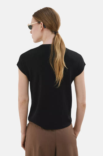 Zwarte top van MANGO met korte mouwen en subtiele textuur, gedragen door een model met bruine broek en zonnebril.