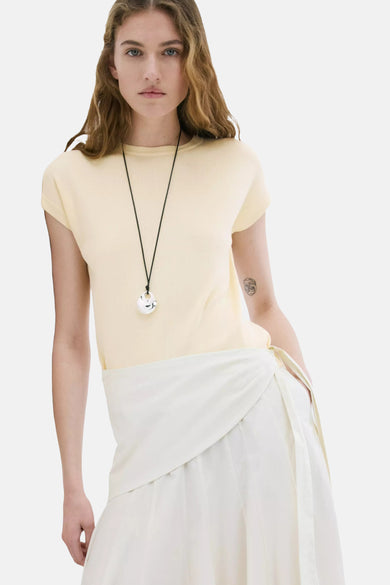 Haut jaune à manches courtes de MANGO, vue de dos sur un mannequin aux cheveux bruns et avec une jupe portefeuille de couleur crème.