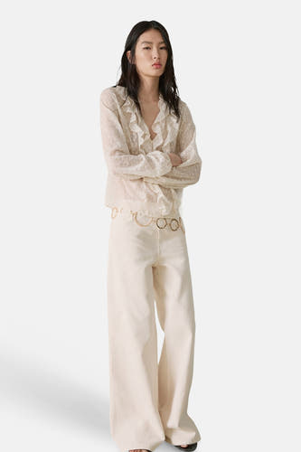 Ecru blouse met lange mouwen van MANGO met ruches en subtiel stippatroon, gecombineerd met wijde broek en gouden ceintuur.