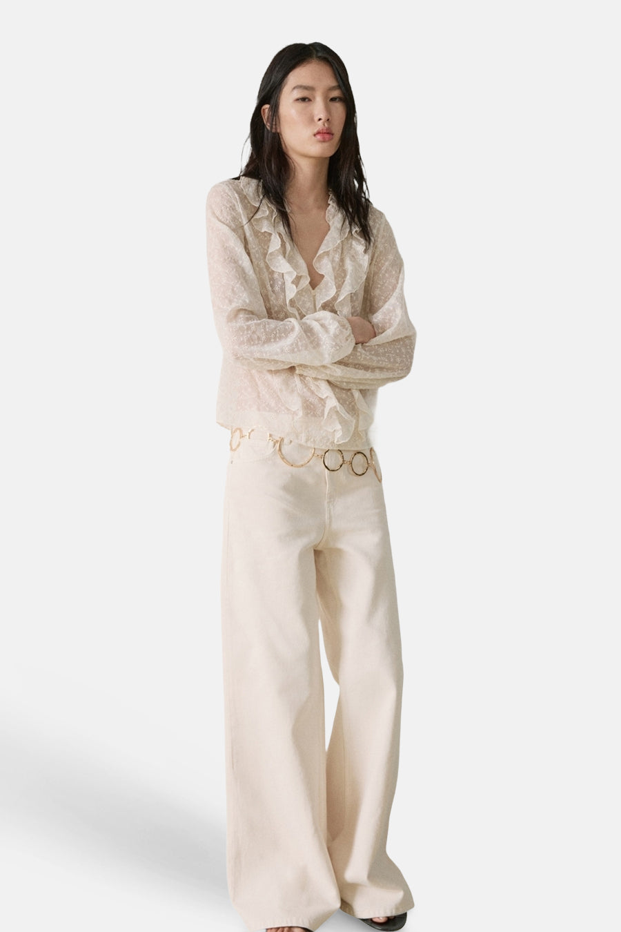 Ecru blouse met lange mouwen van MANGO met ruches en subtiel stippatroon, gecombineerd met wijde broek en gouden ceintuur.