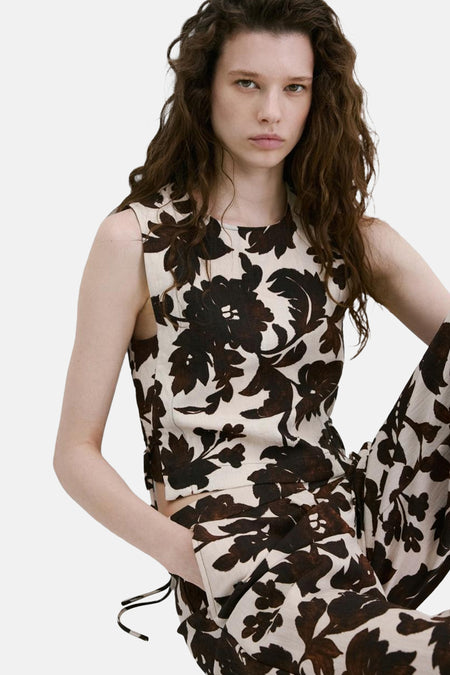 Mouwloze blouse in beige met donkerbruine bloemenprint van MANGO, gedragen door een model met een bijpassende broek.