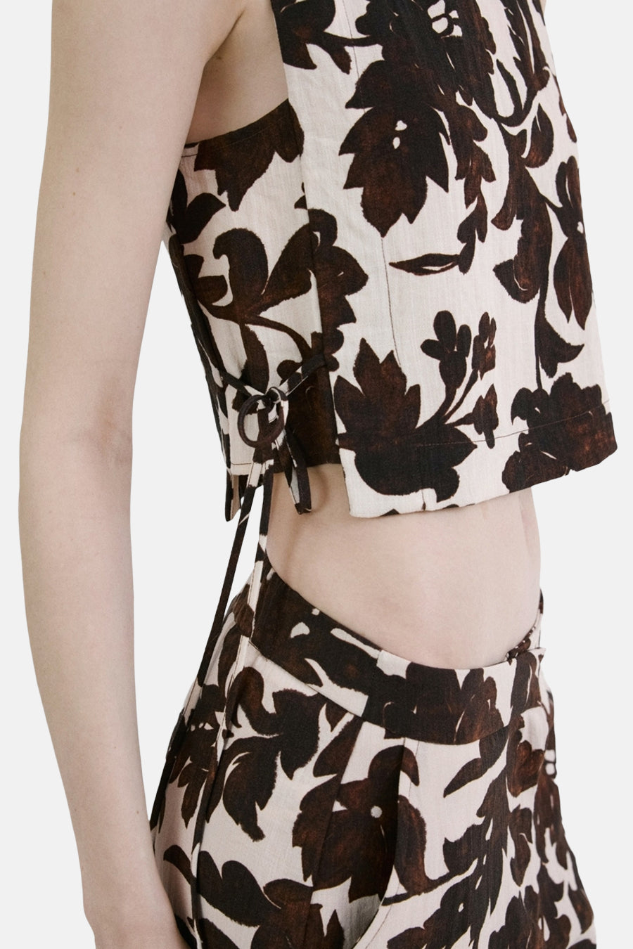 Blouse courte sans manches de couleur crème à motif de feuilles marron de MANGO, avec détails de nœud sur le côté.
