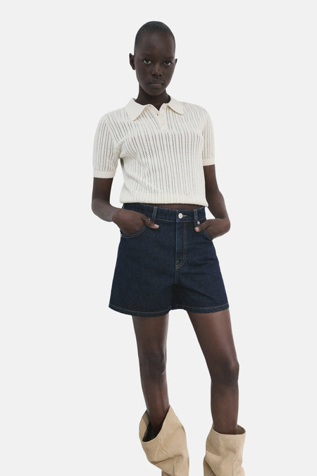 Donkerblauwe denim bermuda shorts van MANGO, gecombineerd met een gehaakte polo en beige laarzen.
