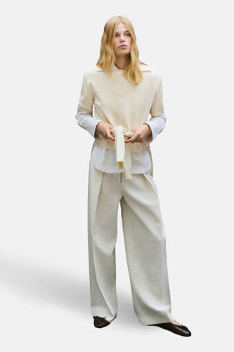 Veste écru avec col rond de MANGO, avec une ceinture à boucle lâche et portée sur un chemisier blanc avec des pantalons larges.