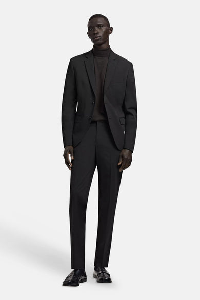 Blazer noire MANGO à deux boutons, portée sur un col roulé foncé avec un pantalon assorti et des mocassins.